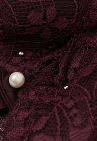 Tessuto di pizzo bordeaux con motivi floreali, caratterizzato da una grande perla bianca e piccoli accenti argentati, superficie testurizzata e dettagli intricati.