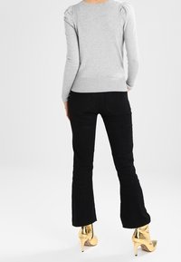 Pull ajusté gris clair avec des manches bouffantes, associé à un pantalon en velours côtelé noir taille haute et des bottes à talons dorées.