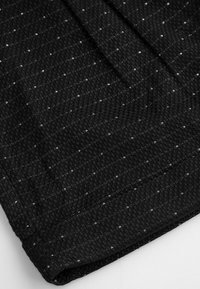 Czarna tkanina z wzorem pepitki z małymi białymi akcentami. Materiał ma teksturowany, tkany wygląd.