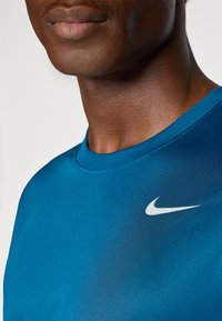 Nike blå sports T-shirt med korte ærmer, rund hals og et hvidt swoosh-logo på venstre brystområde. Glat tekstur.