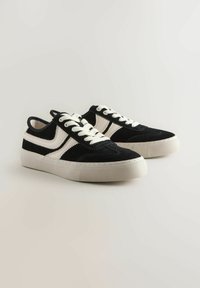 Mustat mokkakengät valkoisilla nahka-asusteilla, pyöreä varvas, kontrastiväriset nauhat, pehmustettu pohja ja teksturoidut kumipohjat.