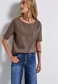 Bruin kortmouwtop van zacht materiaal, met een brede ronde hals, gecombineerd met blauwe wijde jeans. Eenvoudig ontwerp zonder patronen.
