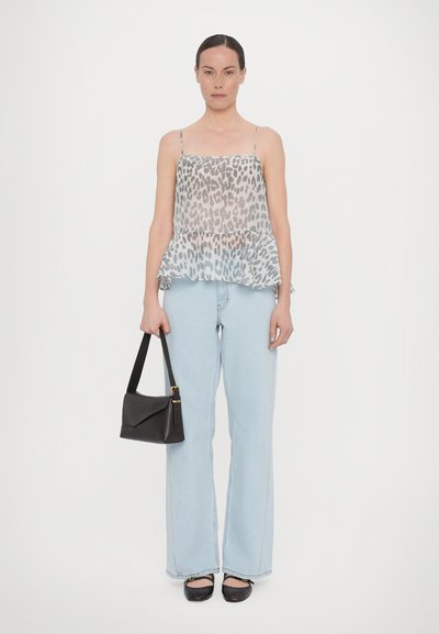 Transparente, ärmellose Bluse mit grauem Leopardenmuster, kombiniert mit hellblauen Schlagjeans. Schwarze Handtasche mit kurzem Griff und strukturierten Ballerinas.