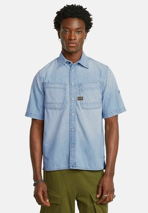 Lichtblauw denim shirt met korte mouwen, twee borstzakken, knoopsluiting aan de voorkant en een label op de linkse zak. Zachte textuur.