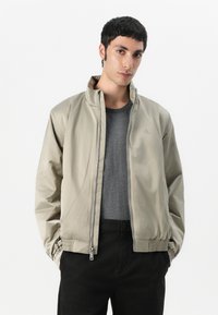 Bežinė bomber jacket su užtrauktuku, stovinčia apykakle, elastingomis rankovėmis ir šoninėmis kišenėmis. pagaminta iš lygaus, lengvo audinio.