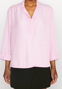 Hellrosa Bluse mit kurzen Ärmeln und Kragen, mit dezenten vertikalen Streifen und legerem Schnitt, kombiniert mit einem schwarzen Rock.