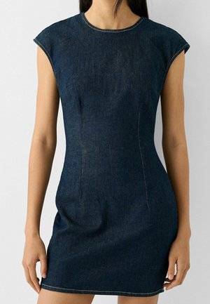 Woman wearing a fitted dark blue sleeveless denim dress with a round neckline and visible stitching details.