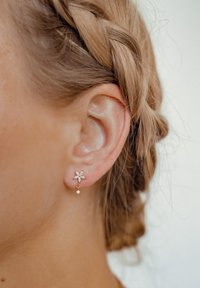 Orecchini floreali in oro con un design a goccia. Il fiore presenta piccole pietre trasparenti e un singolo cristallo pendente per un tocco di dettaglio in più.