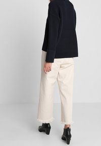 Námořnický žebrovaný svetr, volný střih, spárovaný s krémovými širokými kalhotami s třásněmi na lemu. Černé kotníkové boty dotvářejí celý outfit.