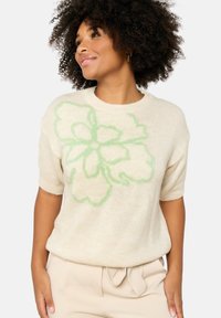 Cream knitted sweater with short sleeves, featuring a large green floral design. Soft texture and relaxed fit, complementing a light outfit.