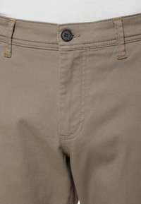 Khakifarbene Baumwollhose mit geradem Schnitt. Verfügt über einen einzelnen Knopfverschluss, orangefarbene Nähte und seitliche Taschen.