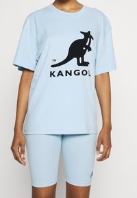 Camiseta de algodón azul claro con mangas cortas y un logo de canguro en negro, combinada con pantalones cortos de bicicleta azules claros a juego.