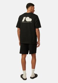Czarny bawełniany t-shirt z krótkim rękawem i dużą grafiką na plecach, w zestawie z czarnymi szortami. Dodatki to białe skarpety i ciemne sandały.