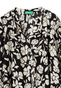Schwarze Bluse mit floralen Mustern in Weiß. Aus leichtem Material hergestellt, mit V-Ausschnitt und Knopfdetails. Der gefältelte Vorderteil sorgt für Textur.