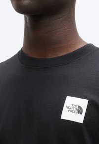 Μαύρο βαμβακερό t-shirt με στρογγυλή λαιμόκοψη, που παρουσιάζει μικρό λευκό τετράγωνο λογότυπο με την επιγραφή "THE NORTH FACE" στην αριστερή πλευρά του στήθους.