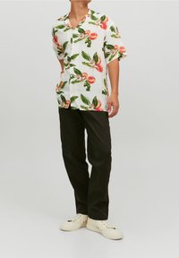 Camisa blanca de manga corta y botones con un estampado de hojas en tonos melocotón y verde, combinada con pantalones negros y zapatillas de color crema.