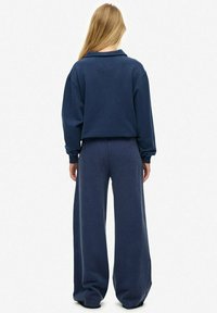 Granatowa, oversize'owa bluza z kołnierzem, zestawiona z szerokimi spodniami o dopasowanym kolorze. Miękka tkanina, luźny krój i minimalistyczne detale.