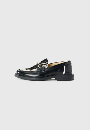 Black and white leather loafers feature a woven design, rounded toe, decorative gold hardware, and a textured black strap with a smooth sole.