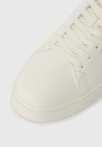 Valge nahast tennisekets, millel on tekstuuriga tallad ja valged paelad, lähedane vaade esiosas ja külgš stitchingule.