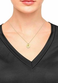 Collana con pendente d'oro e charm circolare inciso con la parola "Famiglia", indossata su una maglietta nera a scollatura a V.