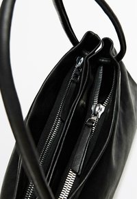 Borsa a mano in pelle nera con chiusura a doppia zip, texture liscia e manici lunghi per un facile trasporto. Le cerniere sono di colore argentato.