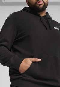 Sweatshirt à capuche noir en coton doux. Il présente une poche avant, un cordon de serrage ajustable et un petit logo sur la poitrine.