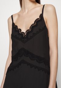 Černá top s tenkými ramínky, zdobený jemnou krajkovou aplikací kolem výstřihu a lemu, vyrobený z měkké látky.