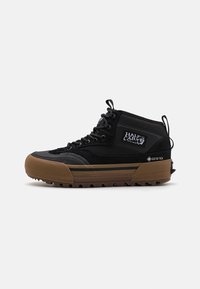 Svarte mid-top sneakers laget av semsket skinn og stoffmaterialer, med gummisåle, logo-patch og GORE-TEX-merke på siden.