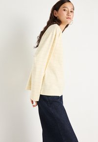 Φωτεινό κίτρινο μακρυμάνικο μπλουζάκι με στενές οριζόντιες ρίγες, σε συνδυασμό με σκούρα τζιν παντελόνια φαρδιάς γραμμής. Μαλακή υφή, άνετη εφαρμογή και στρογγυλή λαιμόκοψη.