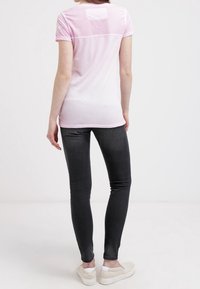 Rosa t-shirt med nätövre rygg, kombinerad med svarta skinny jeans. T-shirten har korta ärmar och en avslappnad passform, tillverkad av lättviktig tyg.