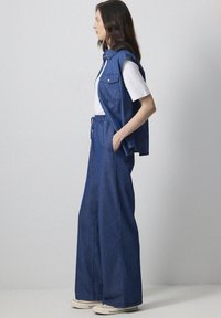 Denim vest and wide-leg pants in blue, paired with a white t-shirt. Vest has button front and pockets; pants feature an elastic waistband.