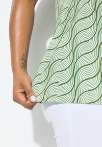 Top bianco e verde a fantasia con linee ondulate, aderente in vita, con un orlo che si solleva delicatamente mostrando una base bianca.