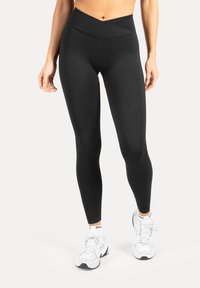 Leggings neri a vita alta con un design incrociato in vita. Realizzati in tessuto elastico, caratterizzati da una texture liscia e una vestibilità aderente.