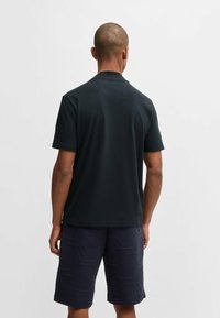Polo shirt noir à manches courtes avec un design simple, associé à des shorts navy avec un motif texturé hexagonal. Le tissu semble lisse.
