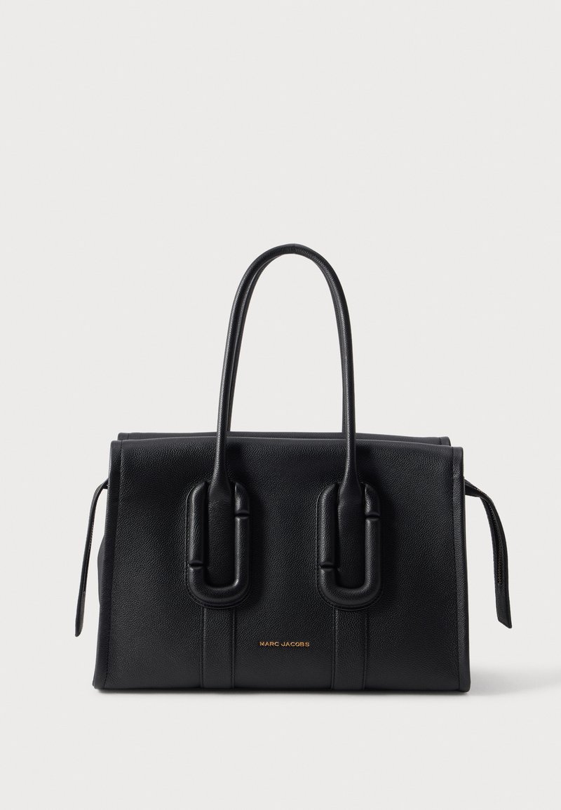 Sac à main en cuir noir texturé avec deux poignées arrondies et logo doré "Marc Jacobs" sur le devant, sur un fond clair uni.