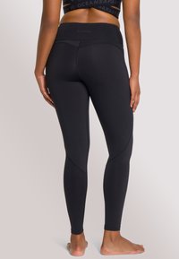 Hoge taille zwarte leggings gemaakt van rekbaar materiaal met platte naden, met een gladde textuur en een contourvormende pasvorm langs de benen.