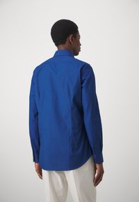 Camicia blu a maniche lunghe con colletto a punta, tessuto liscio e vestibilità su misura. Presenta un orlo curvo e polsini con bottone.