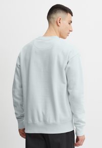 Lichtblauwe sweater met ronde hals, ribgebreide manchetten en zoom, zachte textuur en vlakke naden; heeft een gladde achterkant.