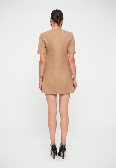 Robe courte ajustée en tissu beige avec une texture lisse. Dotée de manches courtes et d'un ourlet droit, elle est assortie à des chaussures à talons hauts noires.