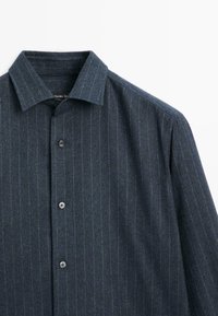 Tmavě modrá pruhovaná košile na knoflíky s klasickým límcem, s malými kulatými knoflíky a strukturální látkou pro zvýraznění detailu.