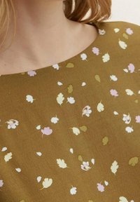 Brauner Stoff mit kleinen, verstreuten Blumenmustern in Hellrosa, Weiß und Grün. Die Textur erscheint weich mit einem leicht matten Finish.