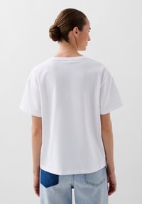 Witte T-shirt met korte mouwen en een ronde hals. Zacht katoen, gladde textuur en een relaxte pasvorm. Gekocht in combinatie met lichtblauwe jeans met een denim patch.