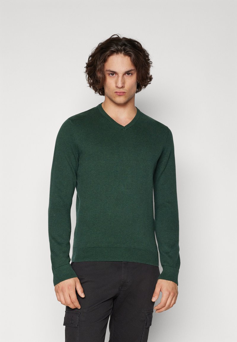 Pulover verde din tricot cu decolteu în V, mâneci lungi și manșete cu nervuri. Materialul pare moale, cu un finisaj texturat și o siluetă ajustată.