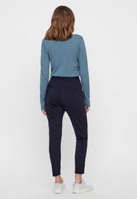 Pantalon bleu marine foncé à coupe fuselée, associé à un haut texturé à manches longues couleur bleu sarcelle. Comprend une ceinture standard et des poches arrière.