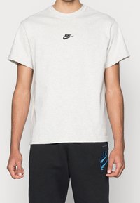 Jasnoszary, krótki rękaw t-shirt wykonany z bawełny, z małym czarnym logo Nike na klatce piersiowej i okrągłym dekoltem.