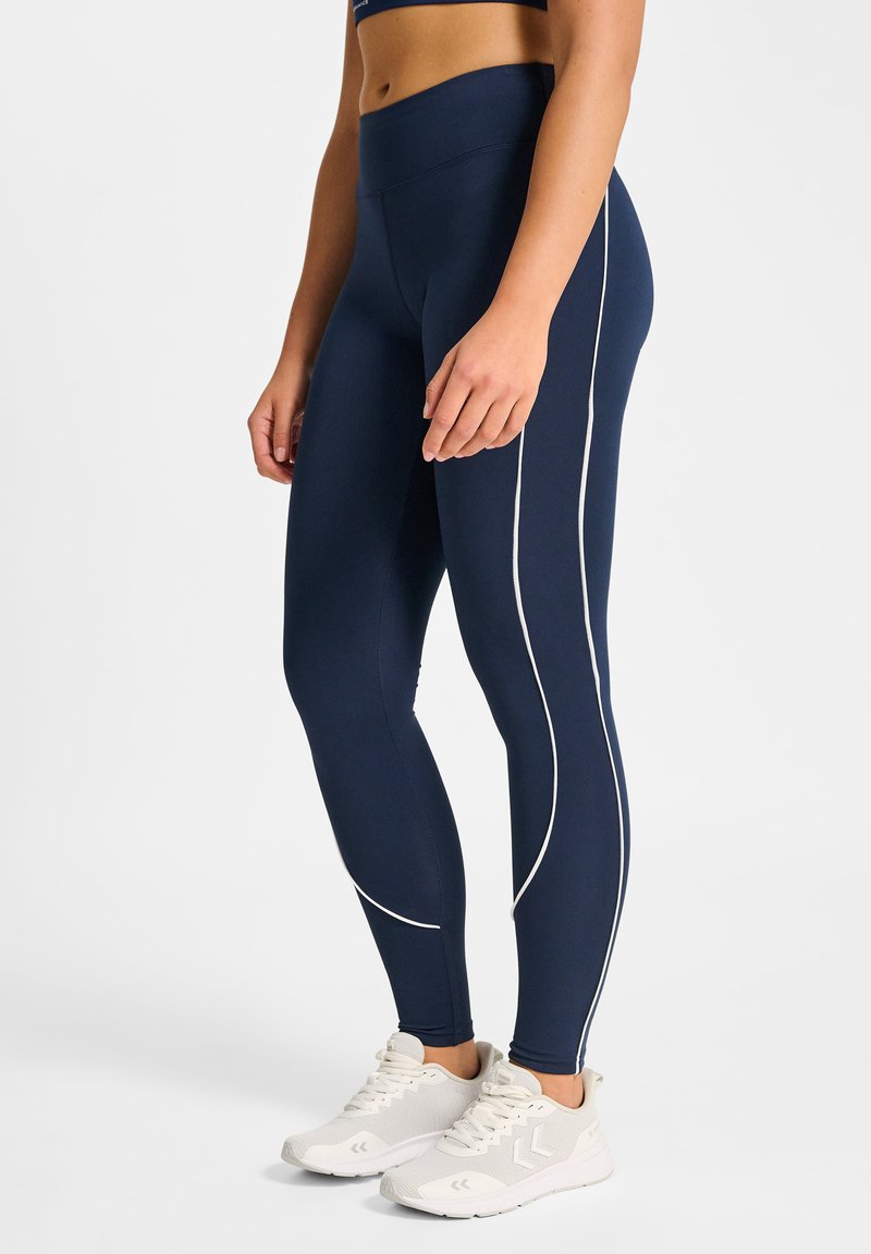 Marinblå leggings med vita sidostrippar, hög midja, slät textur och matchade med ljusa sportskor.