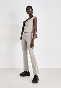 Light gray fitted top and matching flared pants are paired with black chunky sneakers and brown woven bag. Accessories include cat-eye sunglasses.