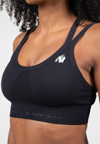 Črna športna modrček z nastavljivimi naramnicami, ki ima mrežasti panel spredaj, teksturirano tkanino in embosiran logotip na elastičnem pasu.