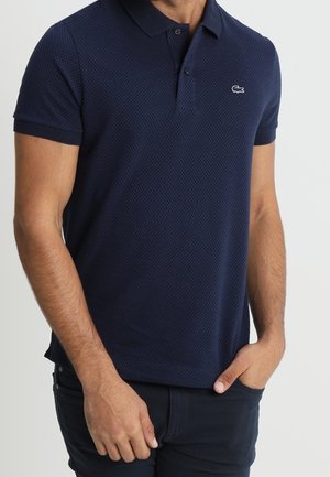 Polo shirt bleu marine à manches courtes avec un motif texturé, col à deux boutons et logo brodé sur la poitrine gauche.