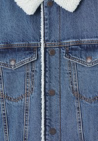 Chaqueta de mezclilla azul con forro sherpa blanco, cierre frontal con botones, bolsillos en el pecho con solapa y botones metálicos, y detalles de costura en naranja.